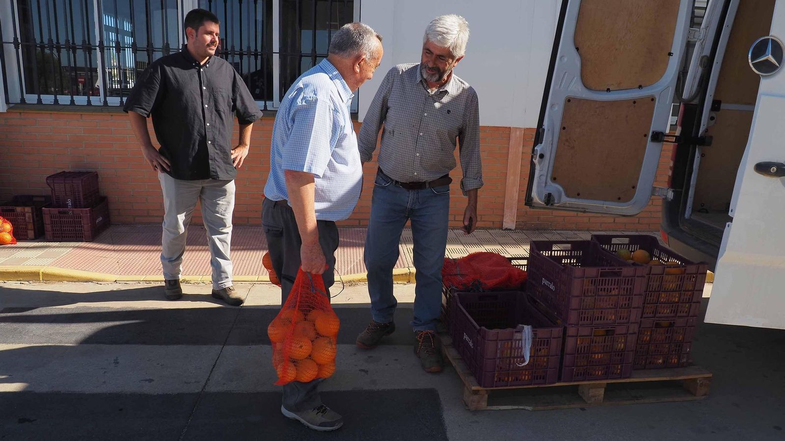 Juan José Gallardo (d) regala dos sacos de naranjas a un vecino