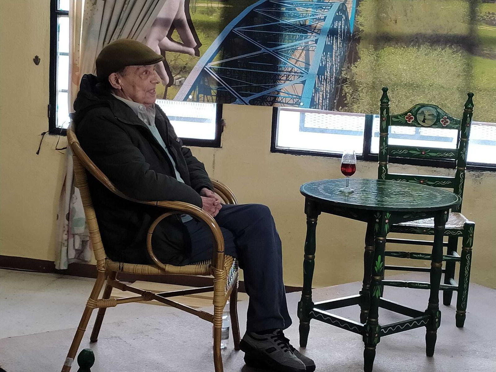 Fernando Belmonte sentado junto a una copa de vino, con una imagen del puente de La Barca de fondo.