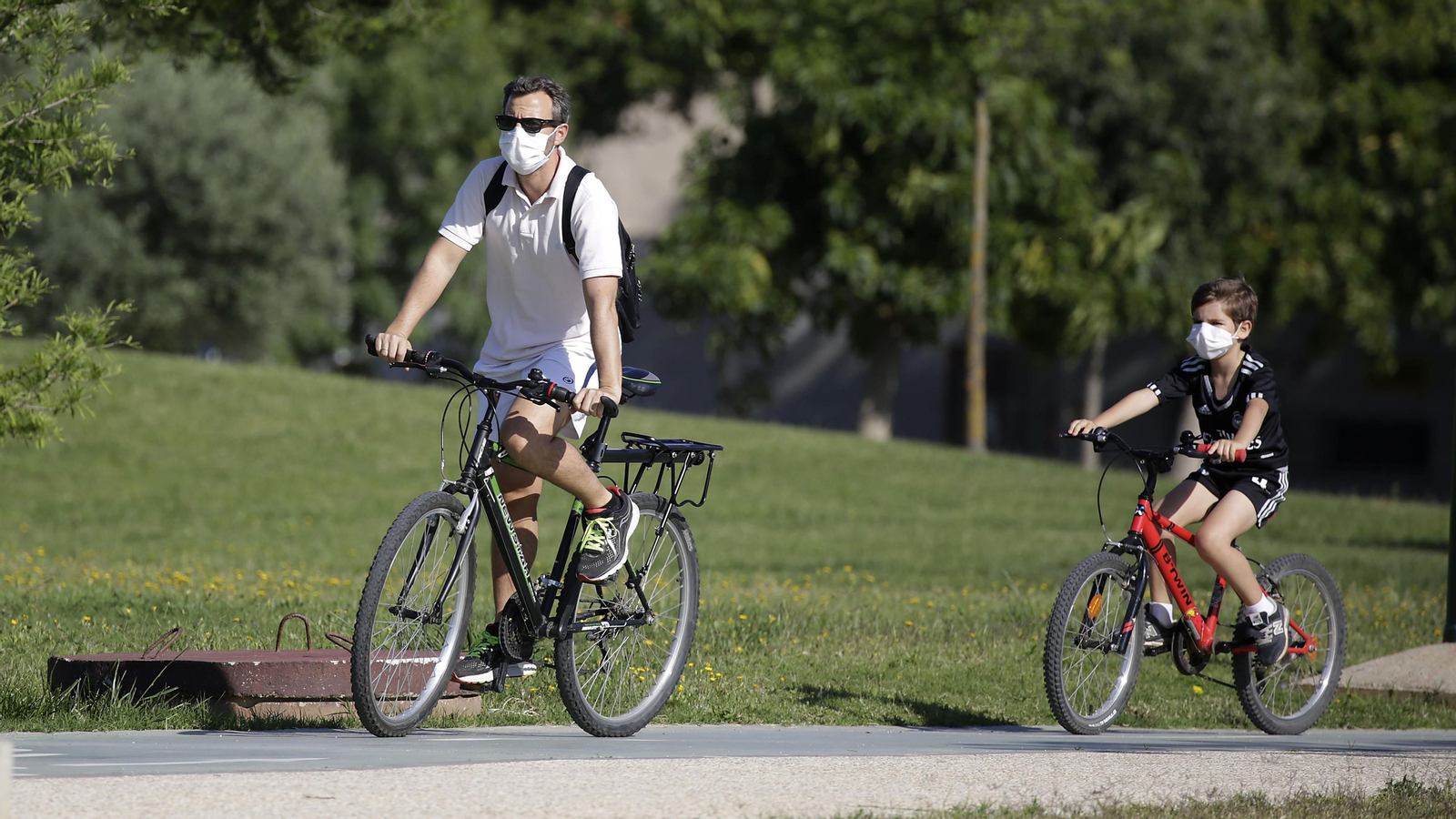 Un padre y su hijo pasean en bicicleta por un parque de Sevilla.