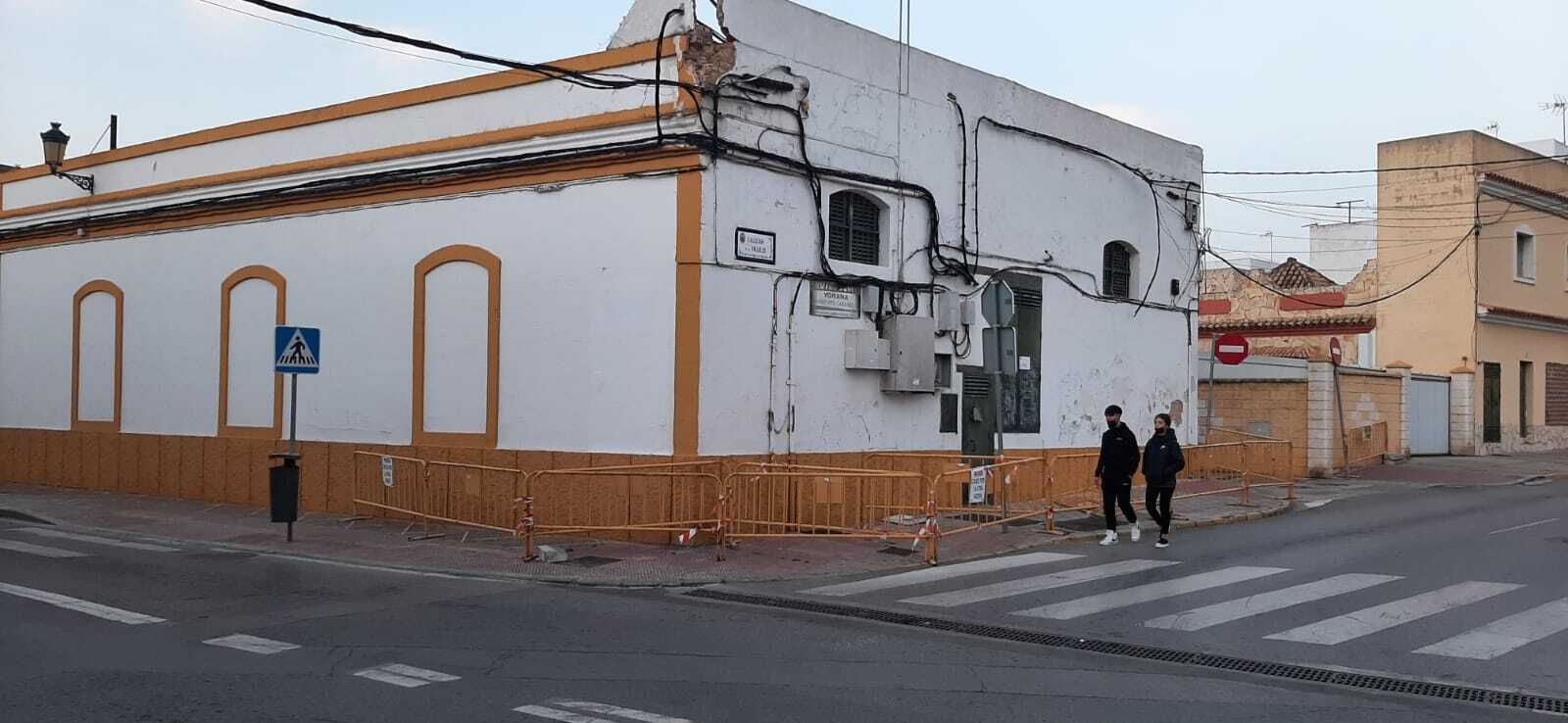 Dos personas caminan por la calzada junto al vallado que ocupa la acera en la esquina de la calle Ancha con el Callejón de los Frailes.