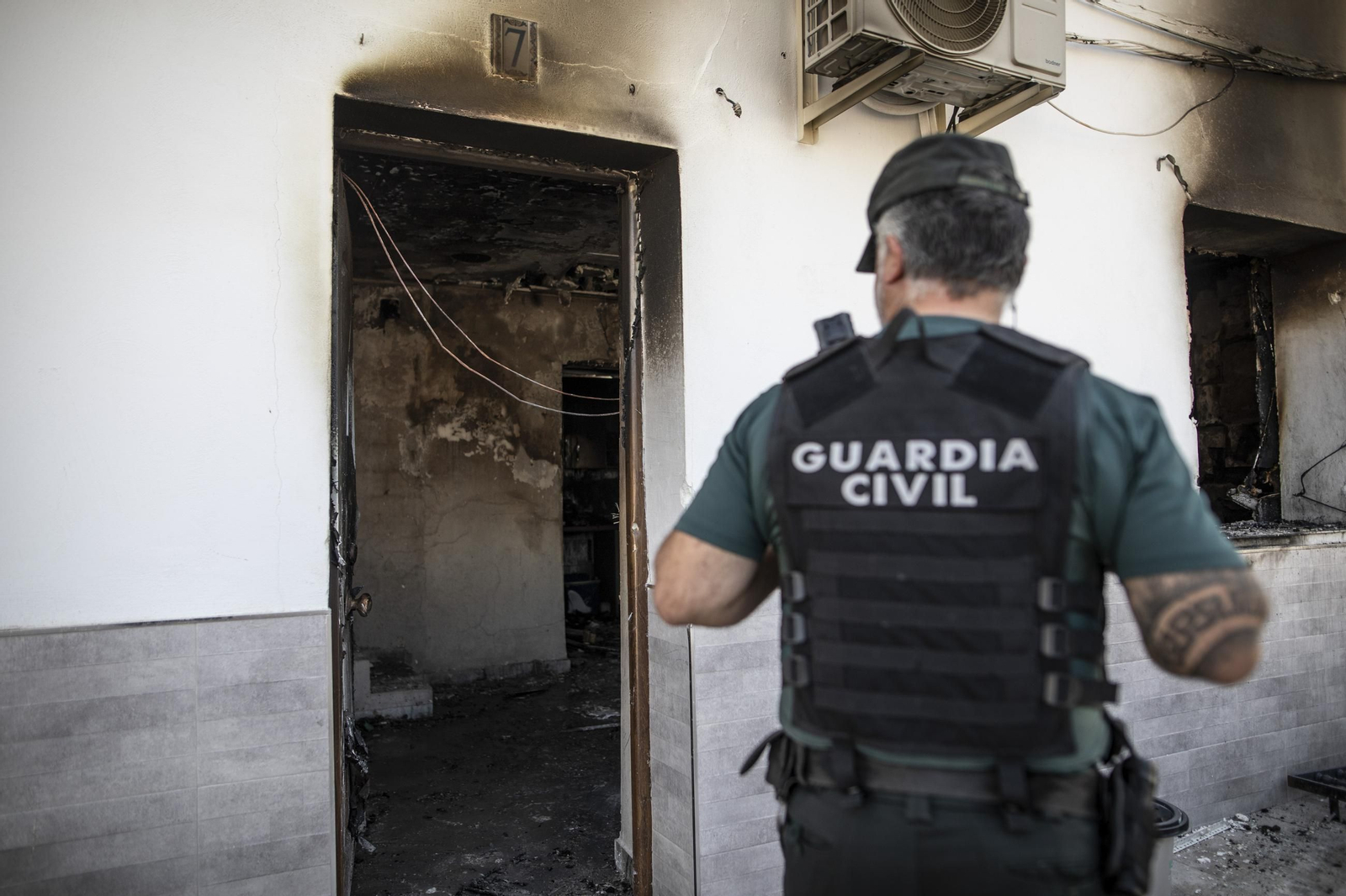 Un agente de la Guardia Civil junto a una de las viviendas incendiadas en Pinos Puente