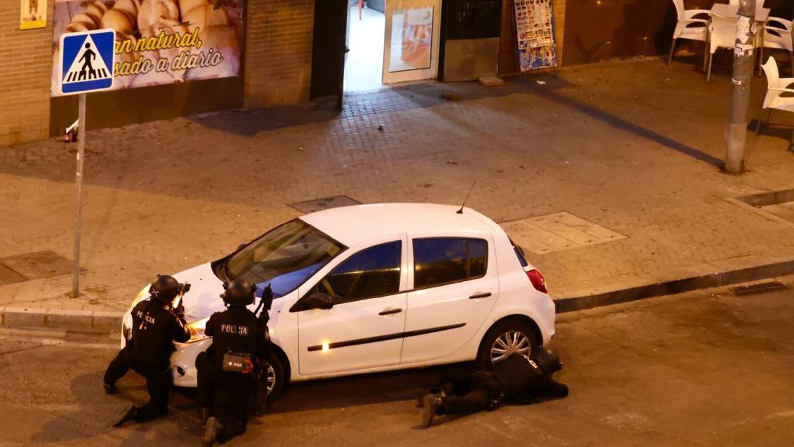 Agentes de la Policía Nacional a cubierto ante la entrada de la panadería.
