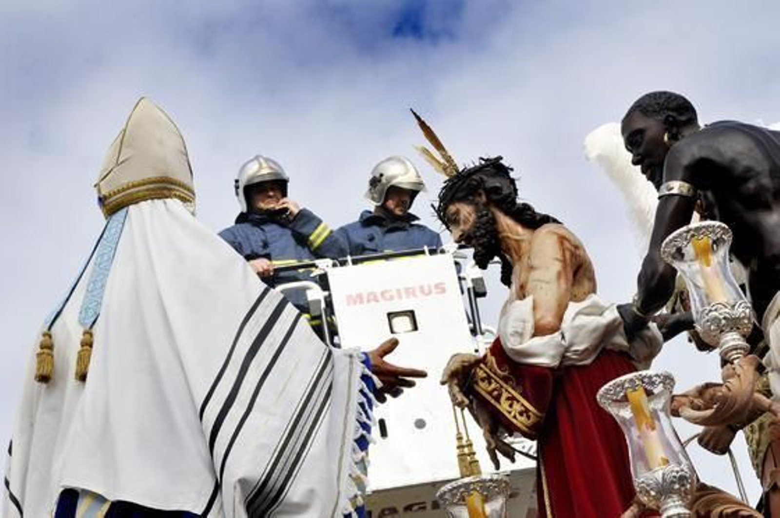 Dos bomberos se 'asoman' al misterio de Jesús de la Paz durante la tradicional ofrenda en Martín Ferrador.

Foto: Manu García
