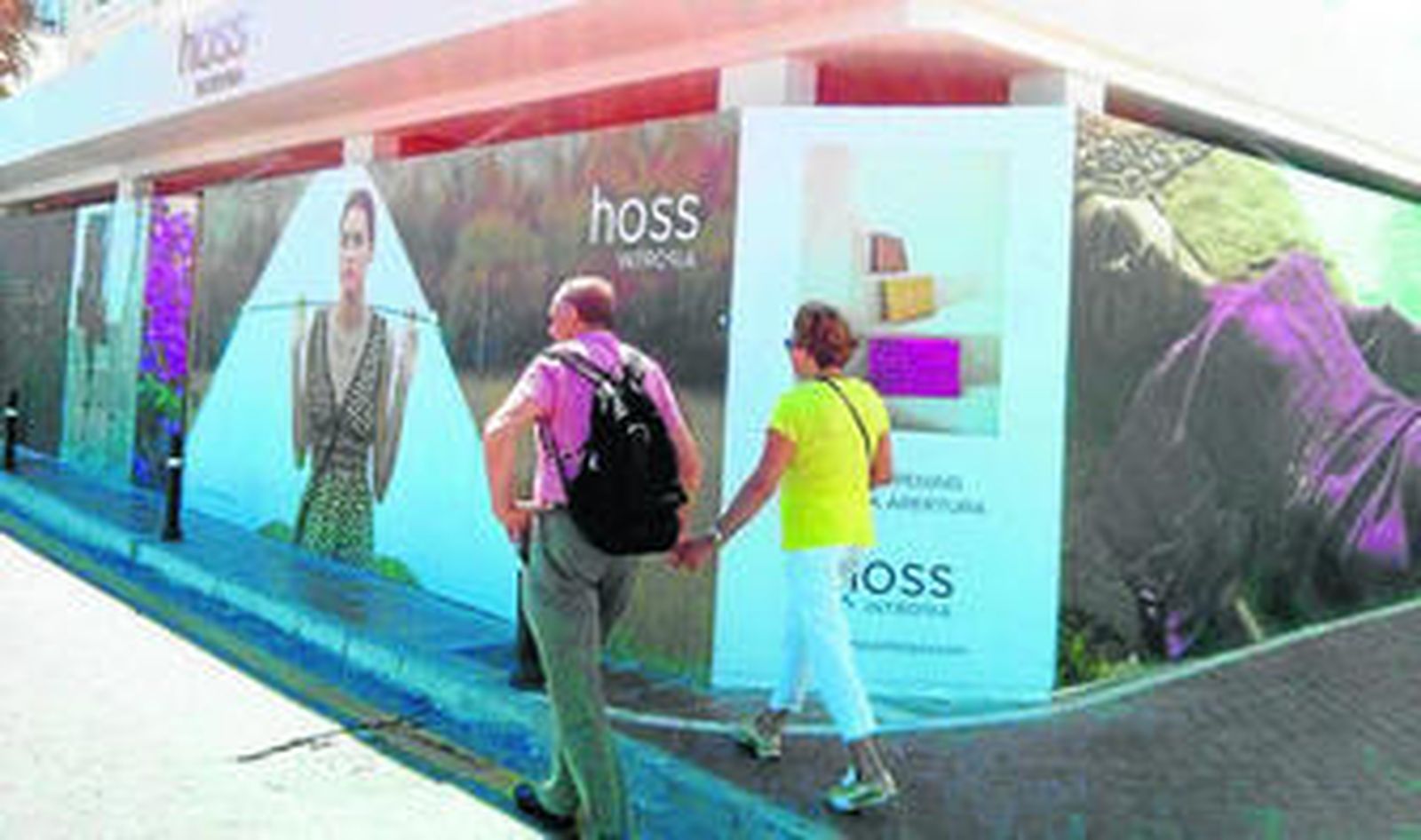 Dos personas pasean junto al local de una tienda de ropa que anuncia su próxima apertura.