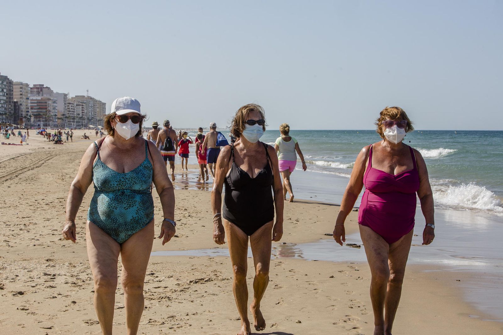 Tres mujeres andan por la orilla en la playa de La Victoria con sus mascarillas.