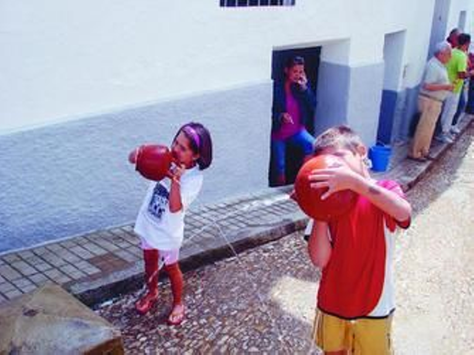 Un niño y una niña utilizan sendos botijos para echarse agua el uno a la otra.