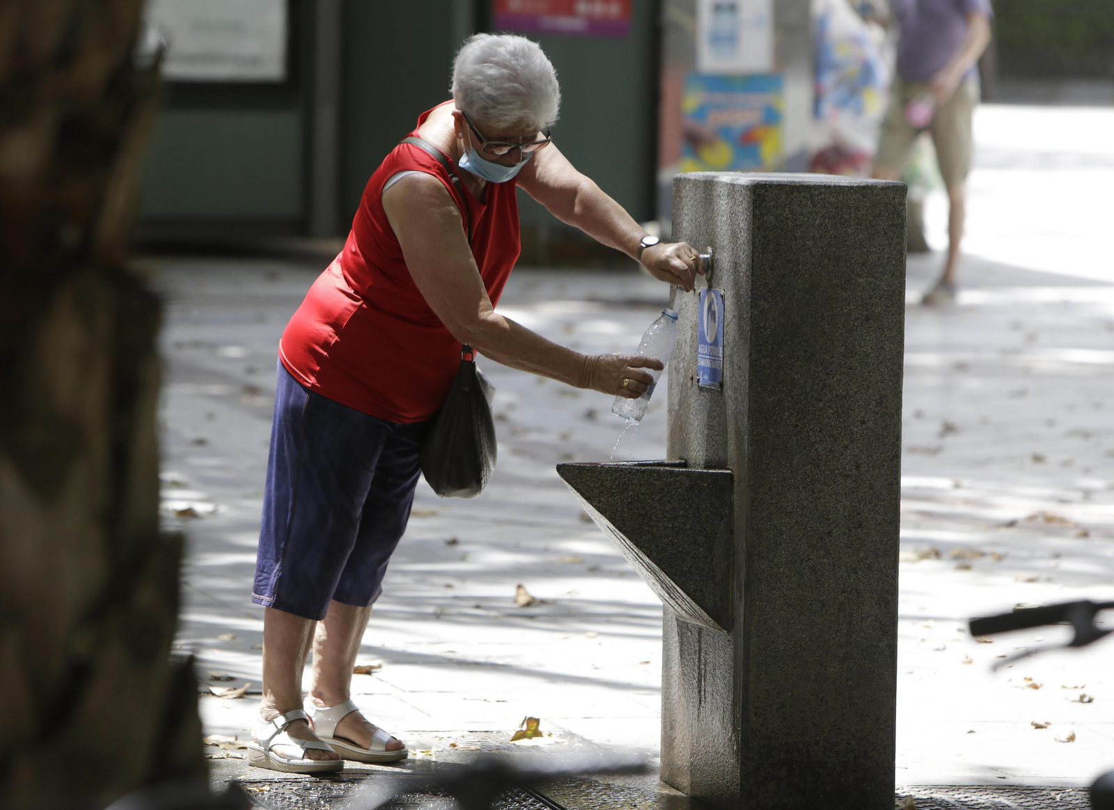 Una mujer se refresca en una fuente de Sevilla.