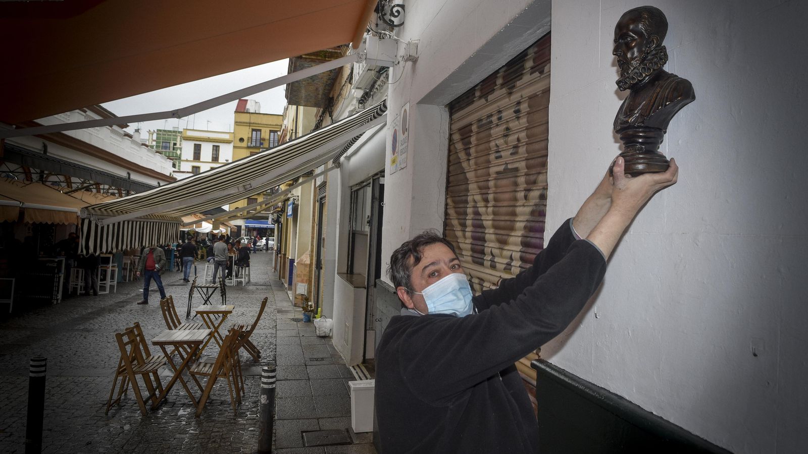 Joaquín Moreno en el exterior de su negocio con el busto de Cervantes.