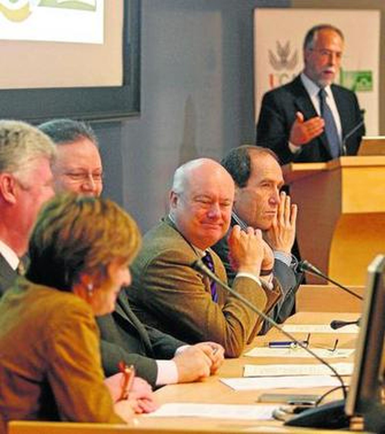 El doctor Micó, al fondo, habla en presencia de los ocupantes de la mesa presidencial tras la firma del convenio.