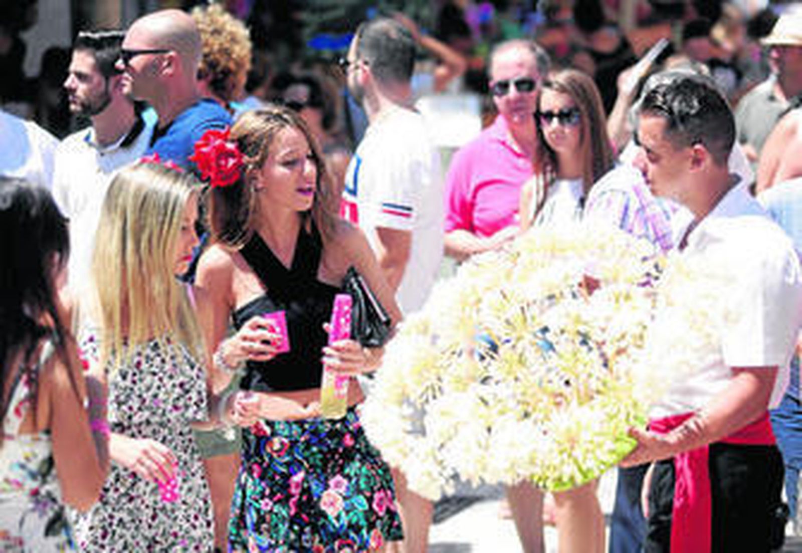 Un biznaguero ofrece su mercancía a dos jóvenes en la Feria de Málaga.