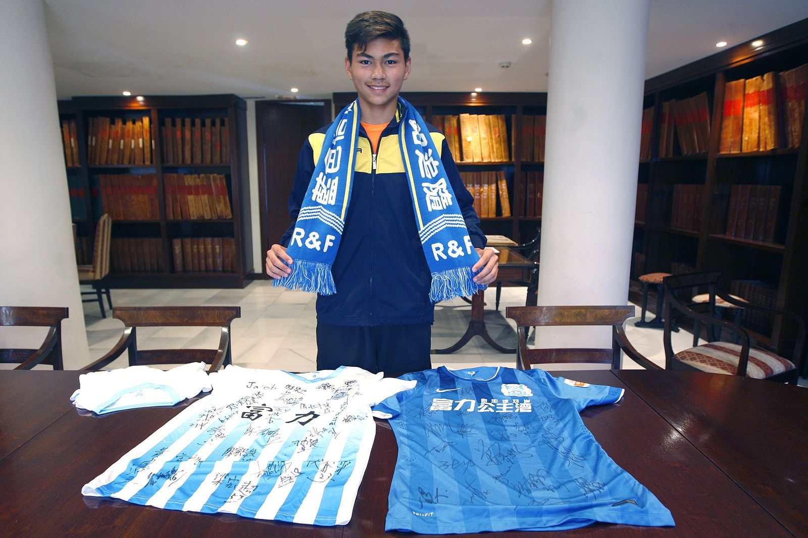 Jesús Carrasco Zhou posa en la hemeroteca de Diario de Cádiz con una bufanda y dos camisetas del que será su equipo en China.