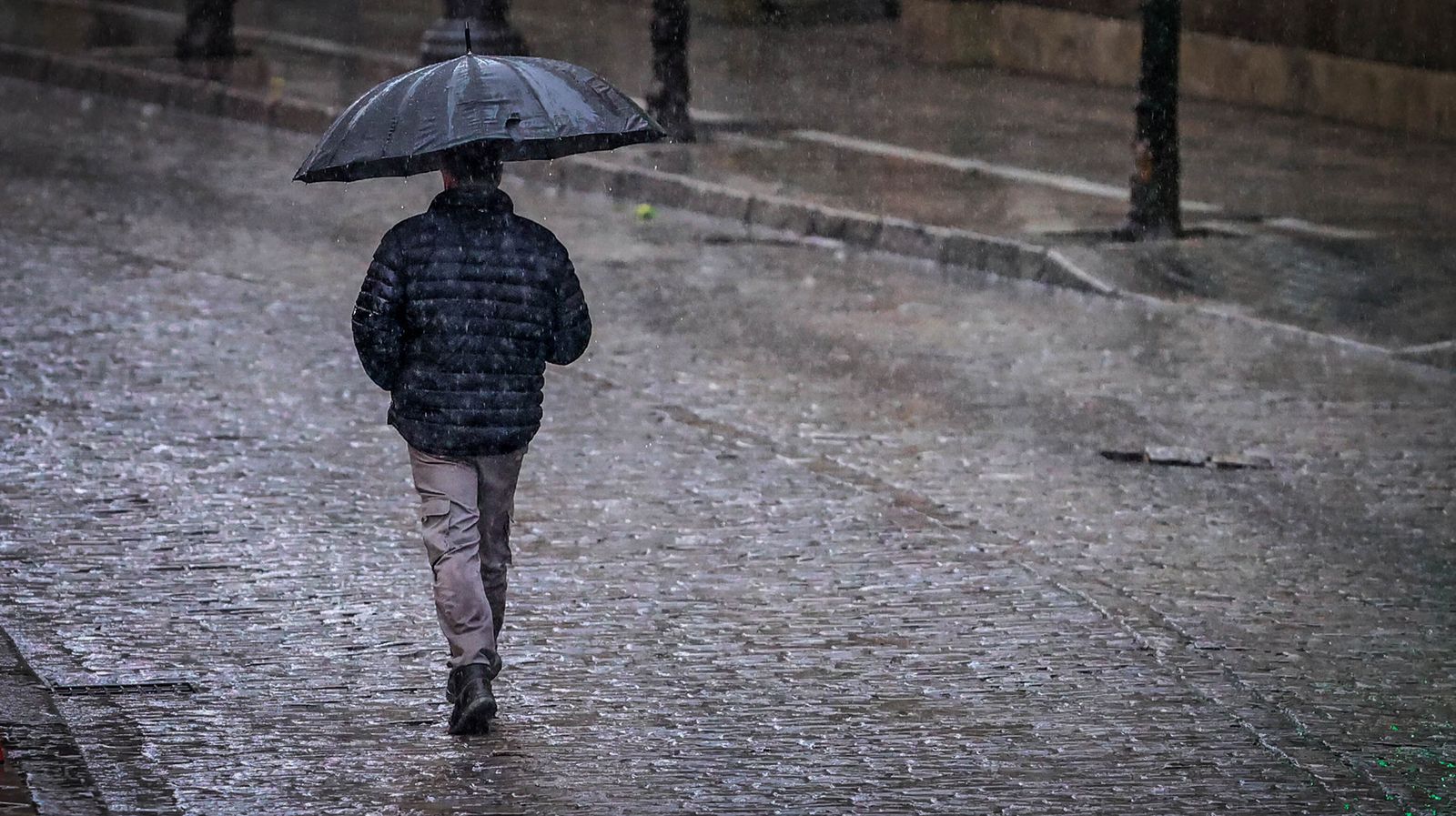 Un hombre caminando bajo la lluvia con un paragüas