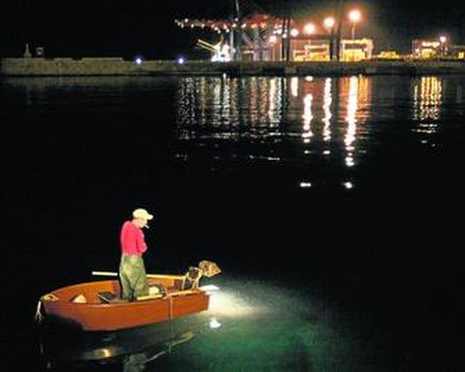 Un pescador faena en el puerto malagueño en plena noche.