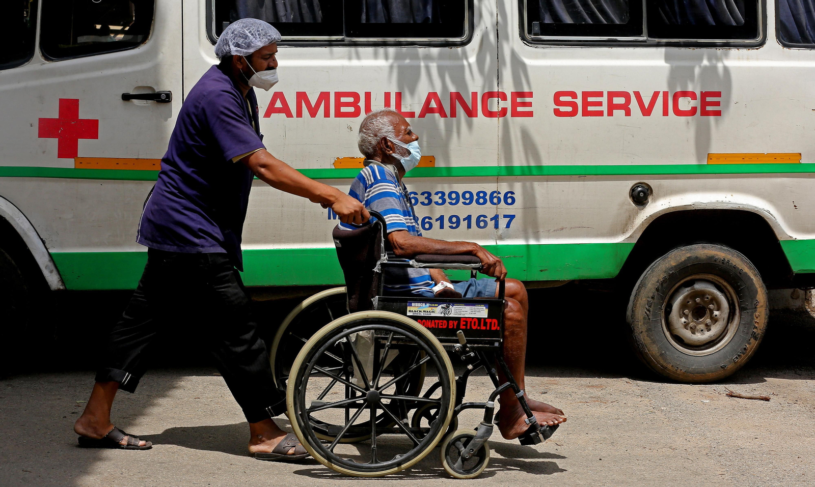 Un hombre lleva en silla de ruedas a un enfermo en Bangalore