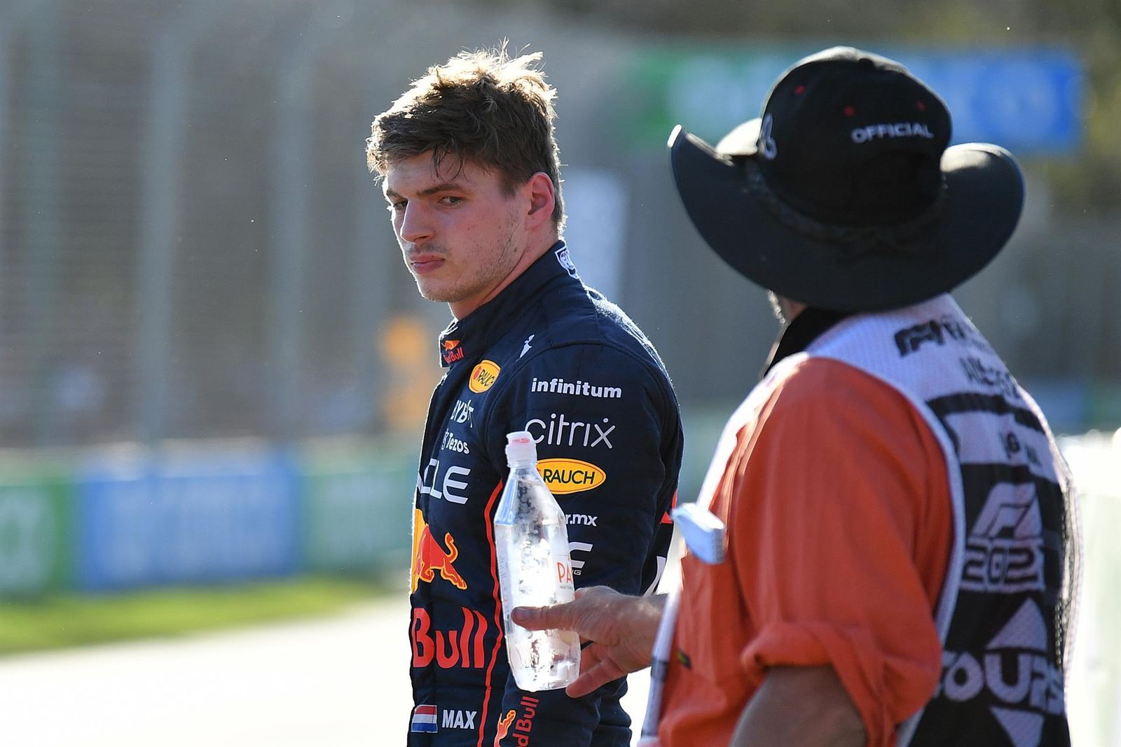 Un comisario de pista ofrece agua a Verstappen, que mira con cara de pocos amigos.