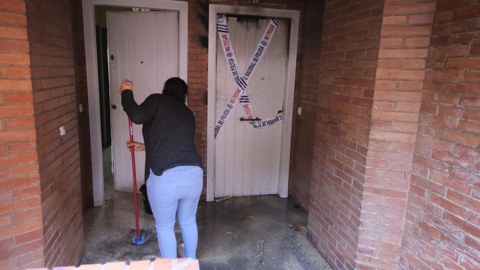 Una vecina achica el agua de los bomberos que ha entrado en su casa.