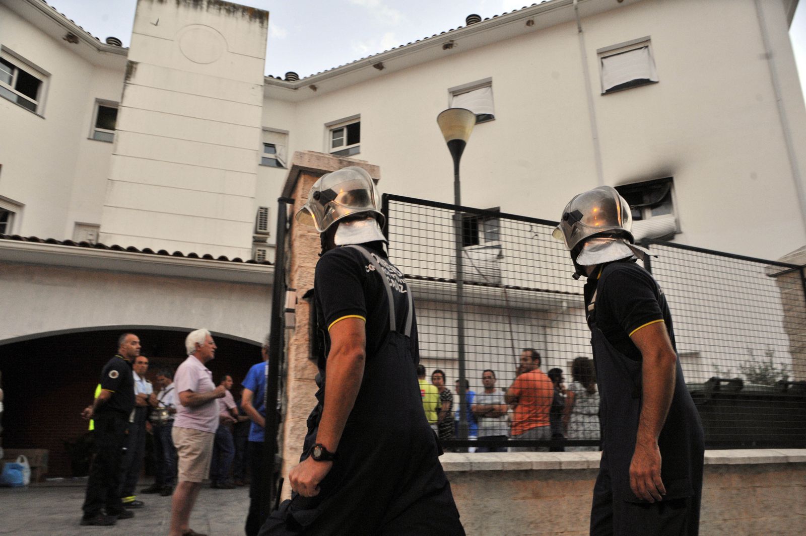 Dos bomberos acceden a la residencia de ancianos de Olvera, con muchos familiares en la puerta. A la derecha se ve en una ventana los restos del incendio.