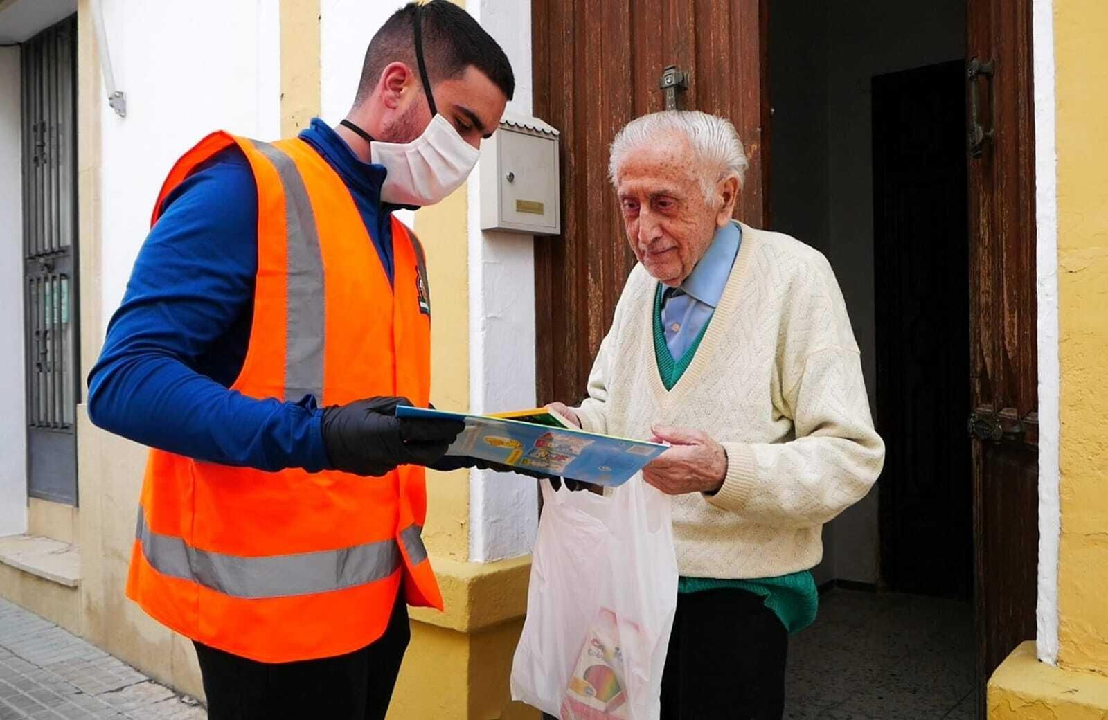 Un voluntario de Protección Civil entrega un kit de entretenimiento a un vecino.