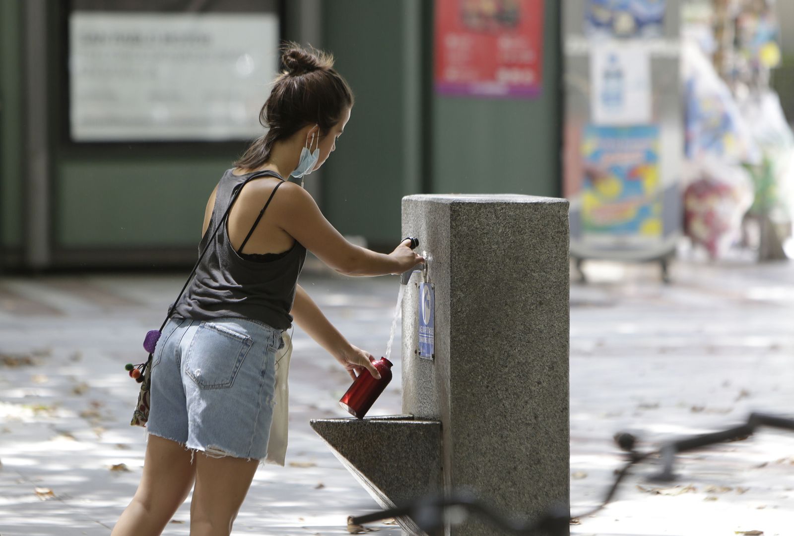 Una joven llena una botella en una fuente del centro.