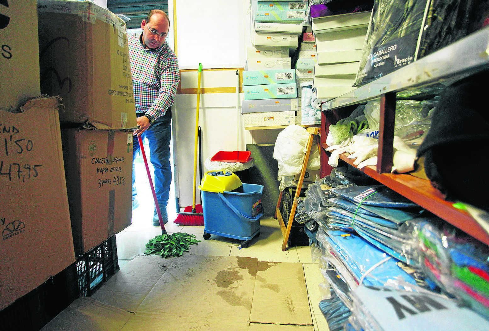 Un comerciante de La Viña recoge el agua de la lluvia que se filtró en su almacén de la calle José Cubiles.