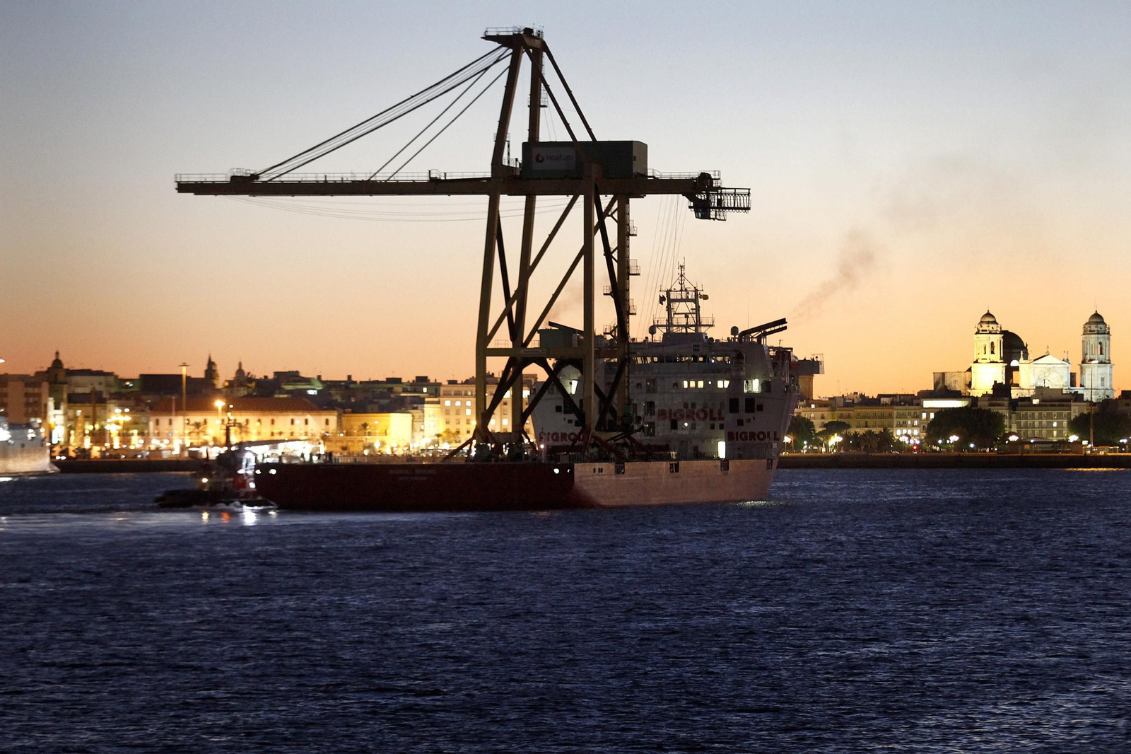 Imagen de archivo de un carguero, con una grúa a cuestas, y con Cádiz iluminado de fondo