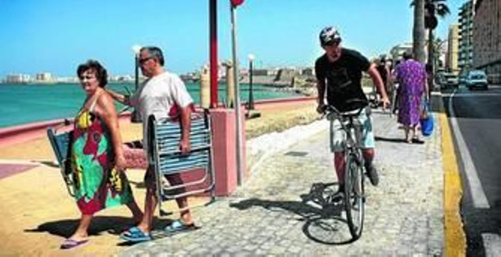 Un ciclista circula por la acera del Paseo Marítimo junto a dos peatones.