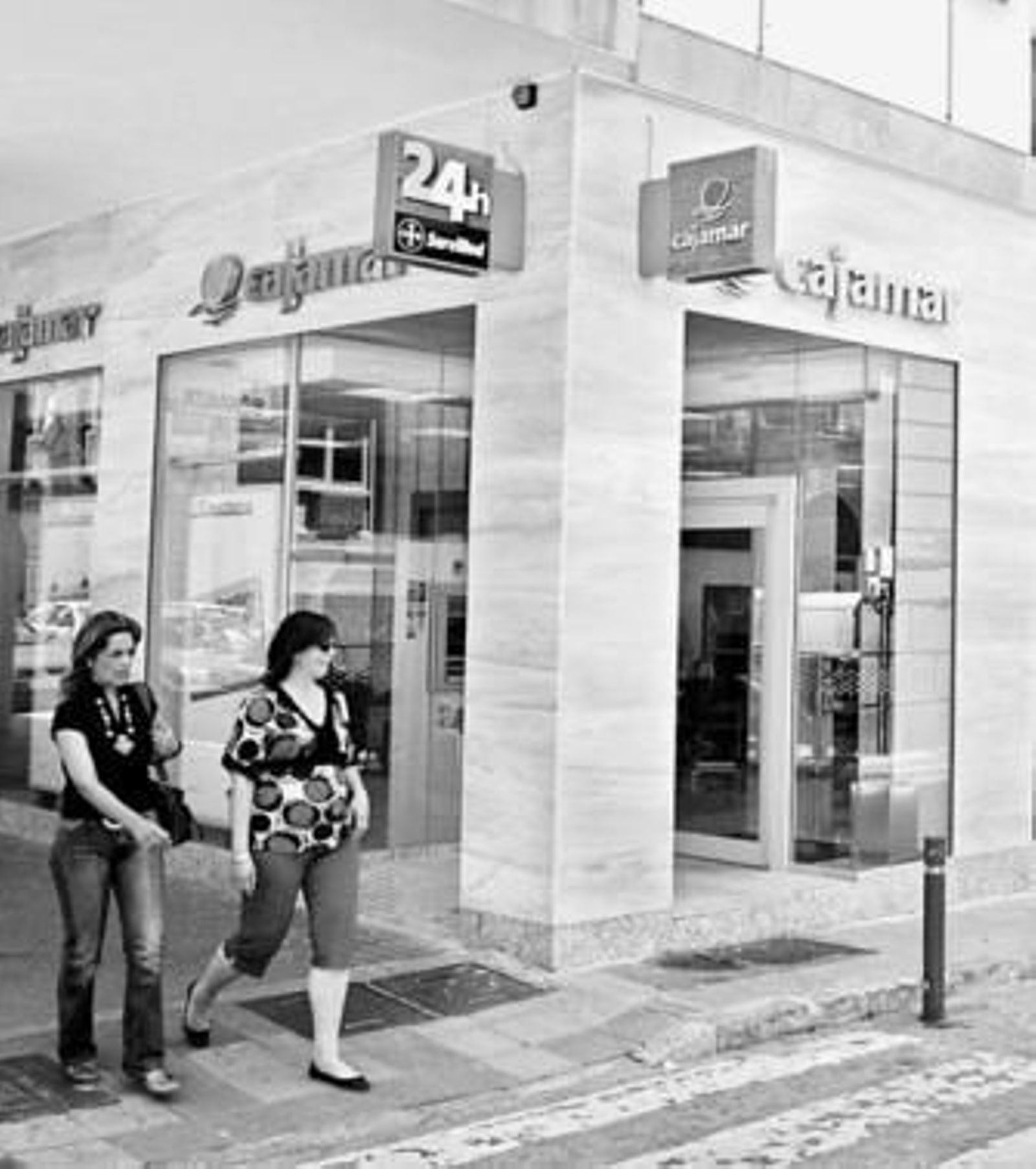 Dos personas pasean por delante de la fachada de la entidad bancaria Cajamar.