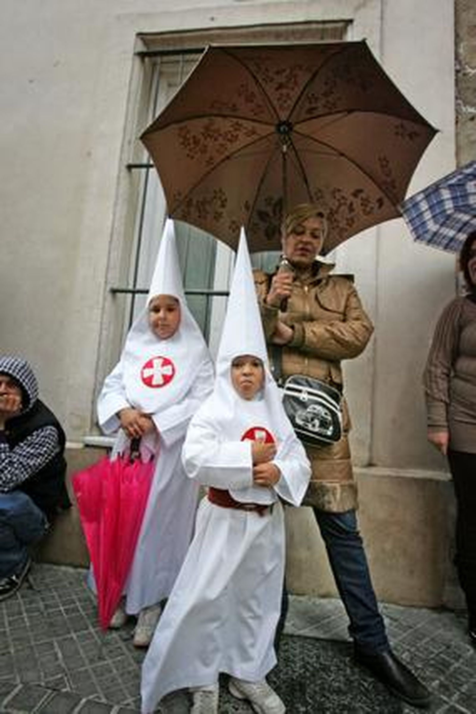 La señora y los niños, paraguas en mano, esperan el desenlace ante la capilla del Cristo del Amor.

Foto: Pascual