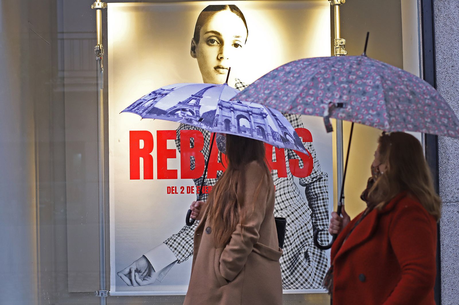 Mujeres con paraguas pasan ayer junto a un anuncio de rebajas en un comercio del centro.