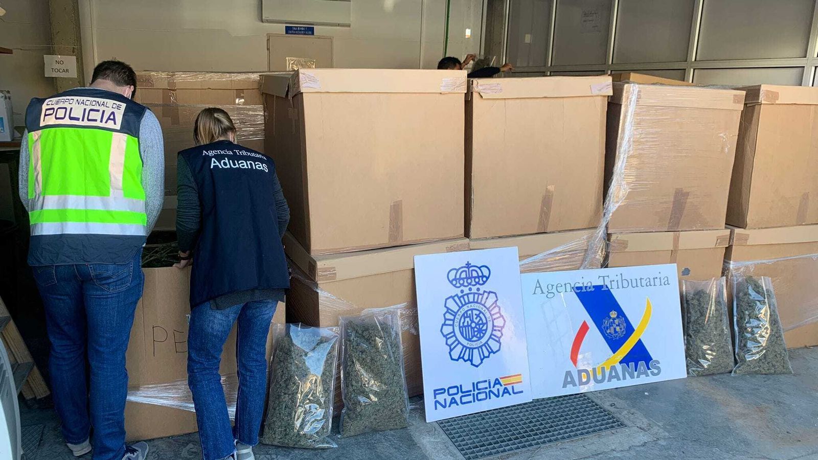 Un policía y una agente de aduanas, con el material intervenido.