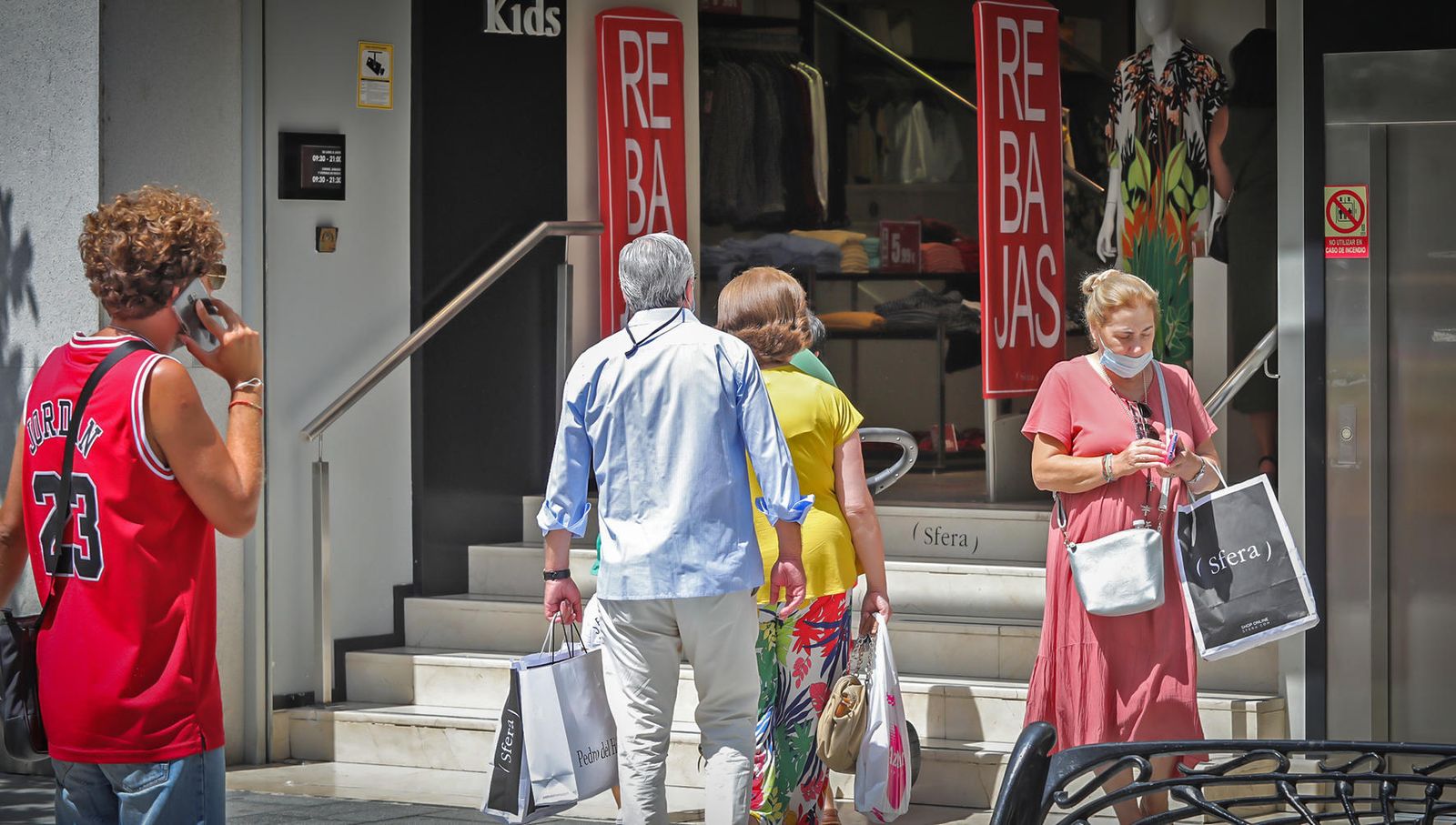 Varias personas con bolsas, junto a un comercio del centro.