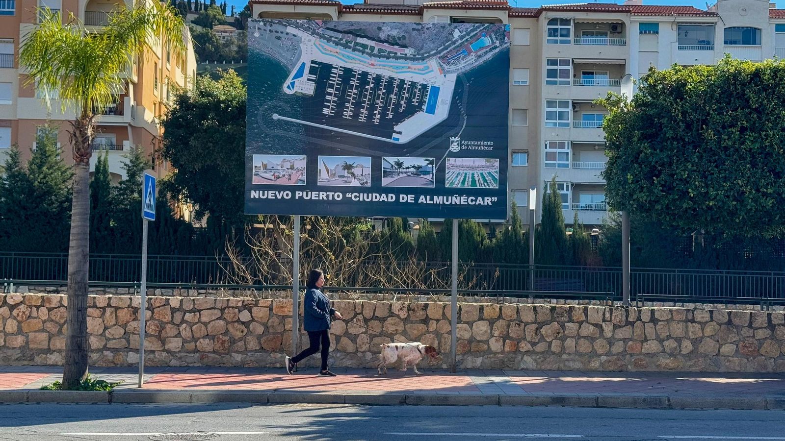 Una persona pasea por Almuñécar con un cartel anunciando el proyecto del puerto deportivo