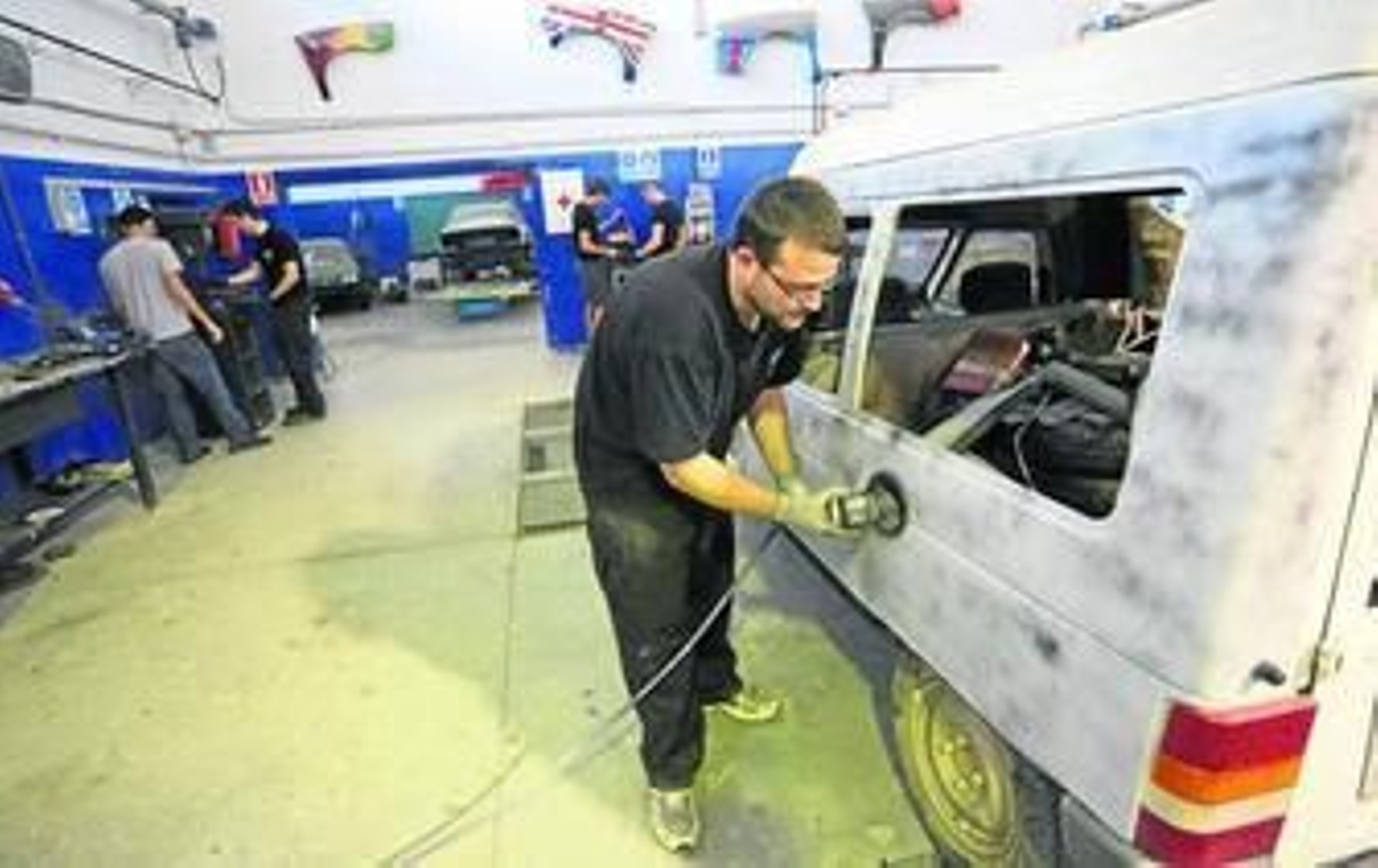 Un alumno lija la chapa de un vehículo.