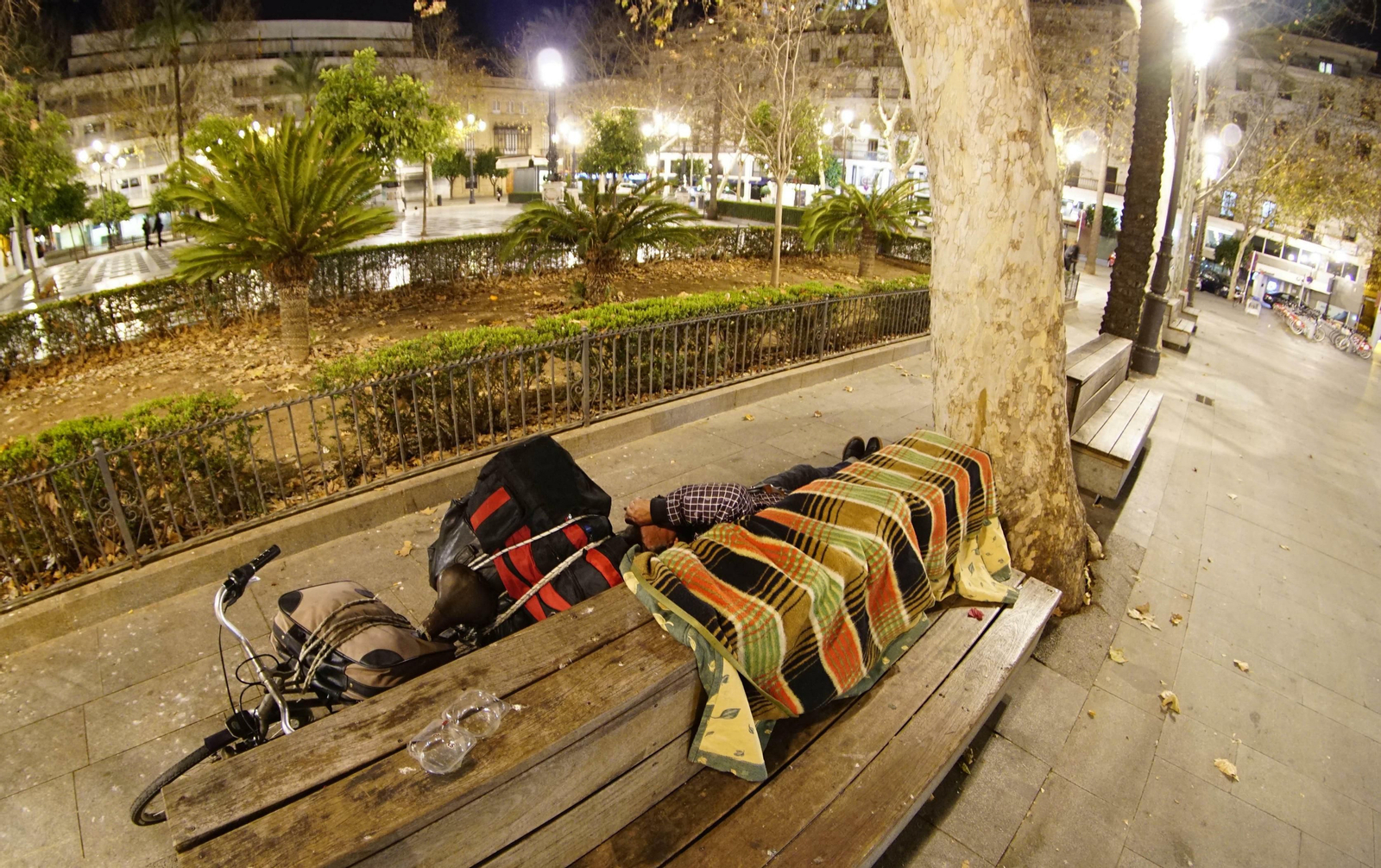 Un transeúnte duerme sobre un banco de la Plaza Nueva.