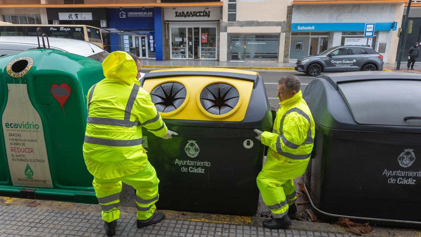 Operarios recolocan contenedores volcados por el fuerte viento que reina este martes en Cádiz.
