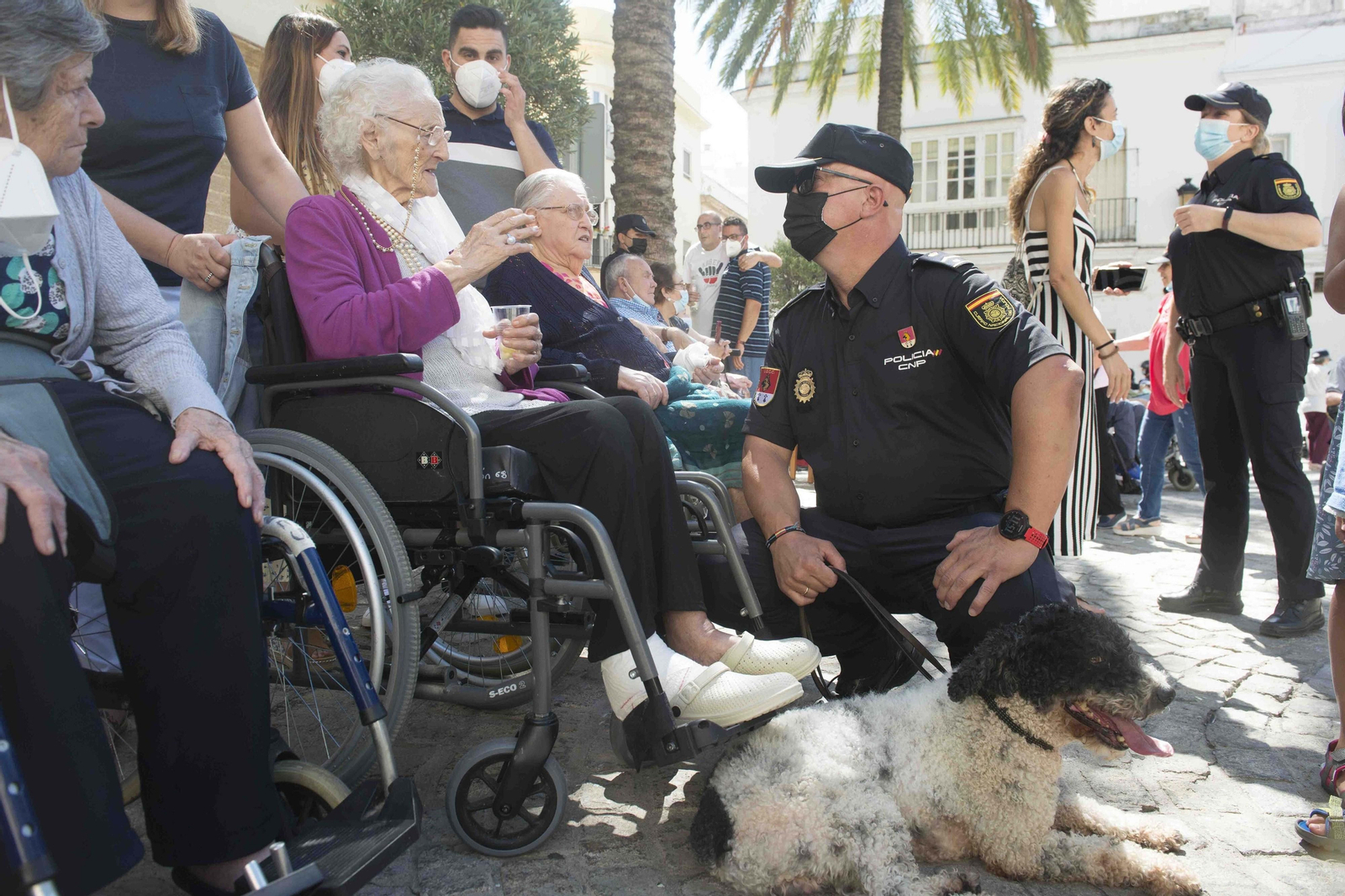 Un agente conversa con una de las personas mayores, con uno de los perros policía a sus pies.a