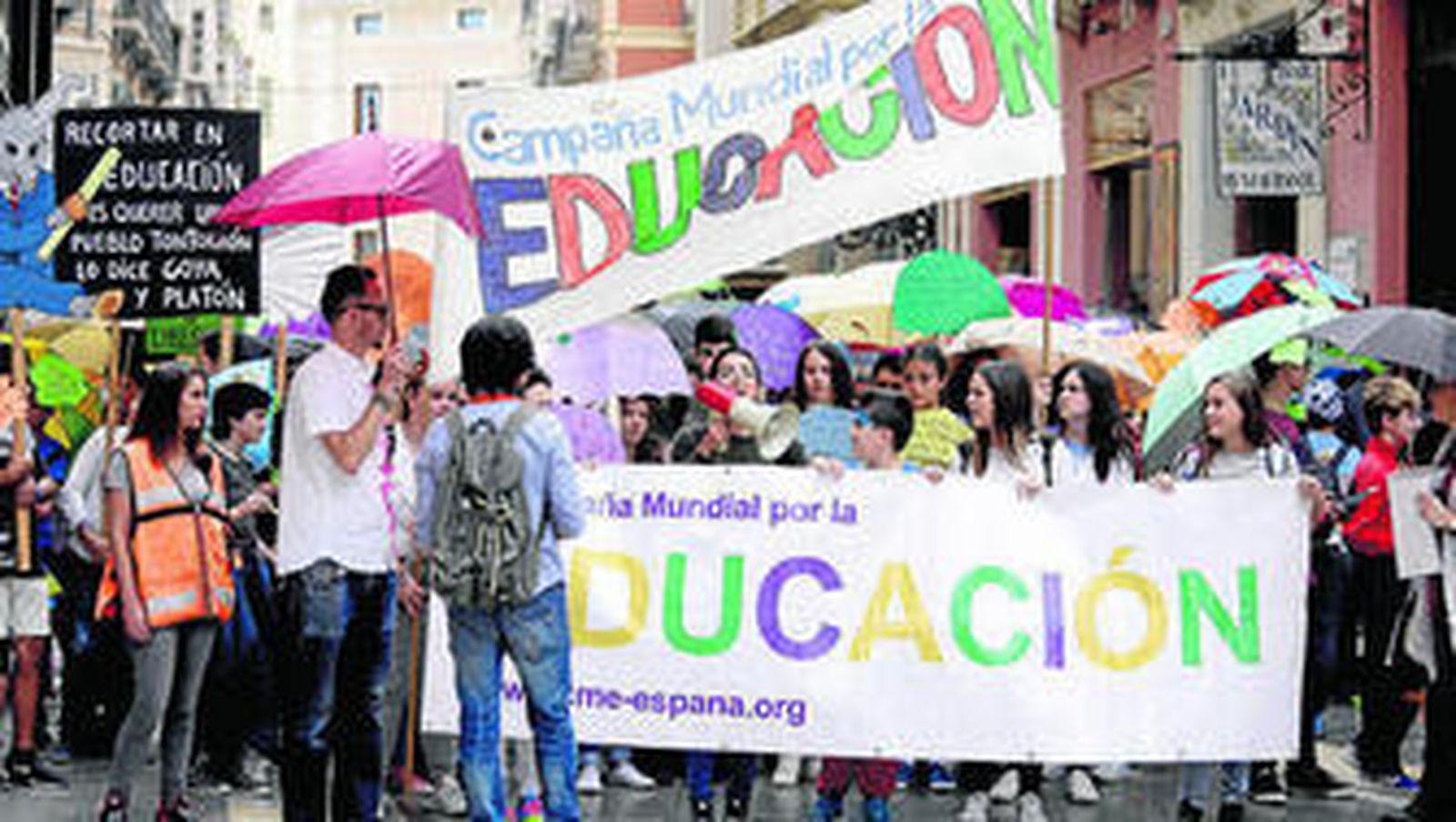 Cabeza de la manifestación con jóvenes junto a las pancartas y los paraguas.