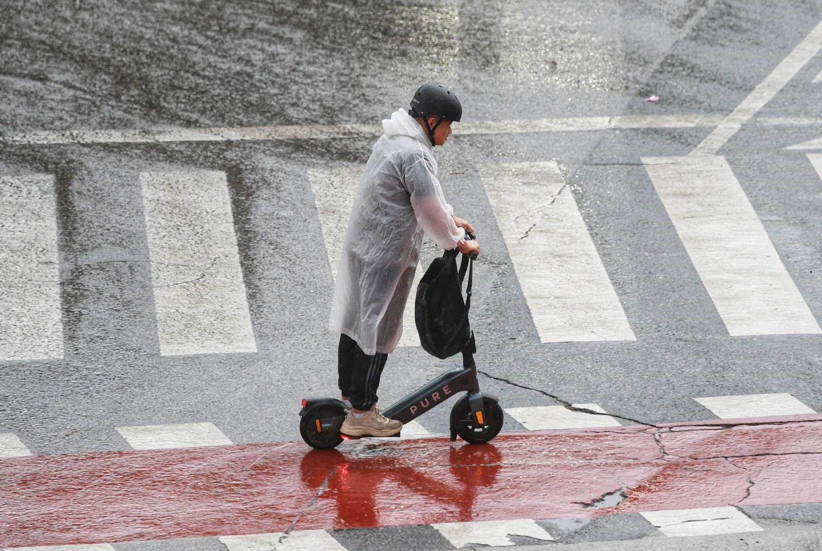 Un joven en patinete durante un día de lluvia en Málaga.