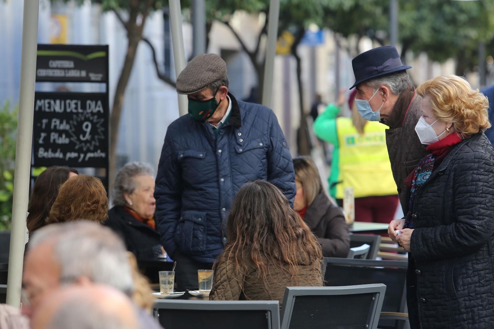 Ciudadanos con la mascarilla puesta conversan con clientes sin la protección sentados en la terraza de un bar