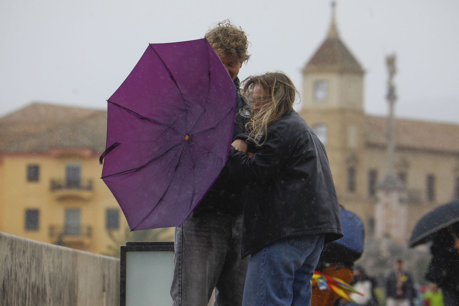 Dos personas sujetan un paraguas golpeado por el viento.