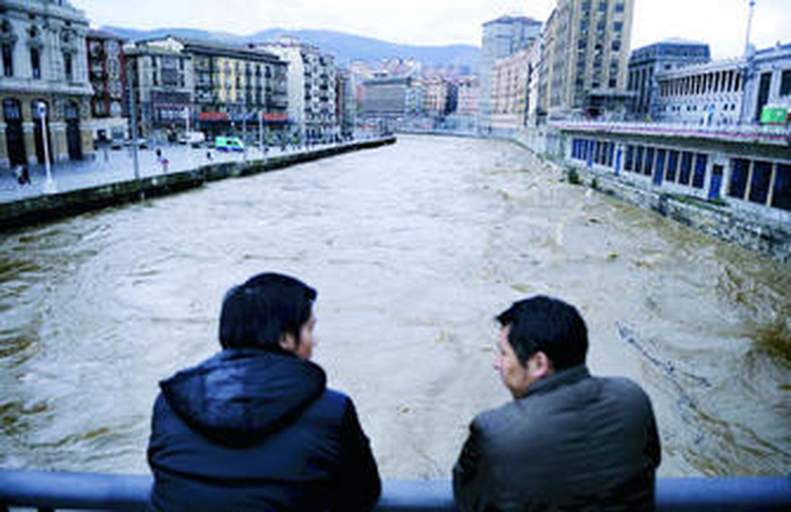 Dos jóvenes observan la crecida del cauce del Nervión a su paso por Bilbao.