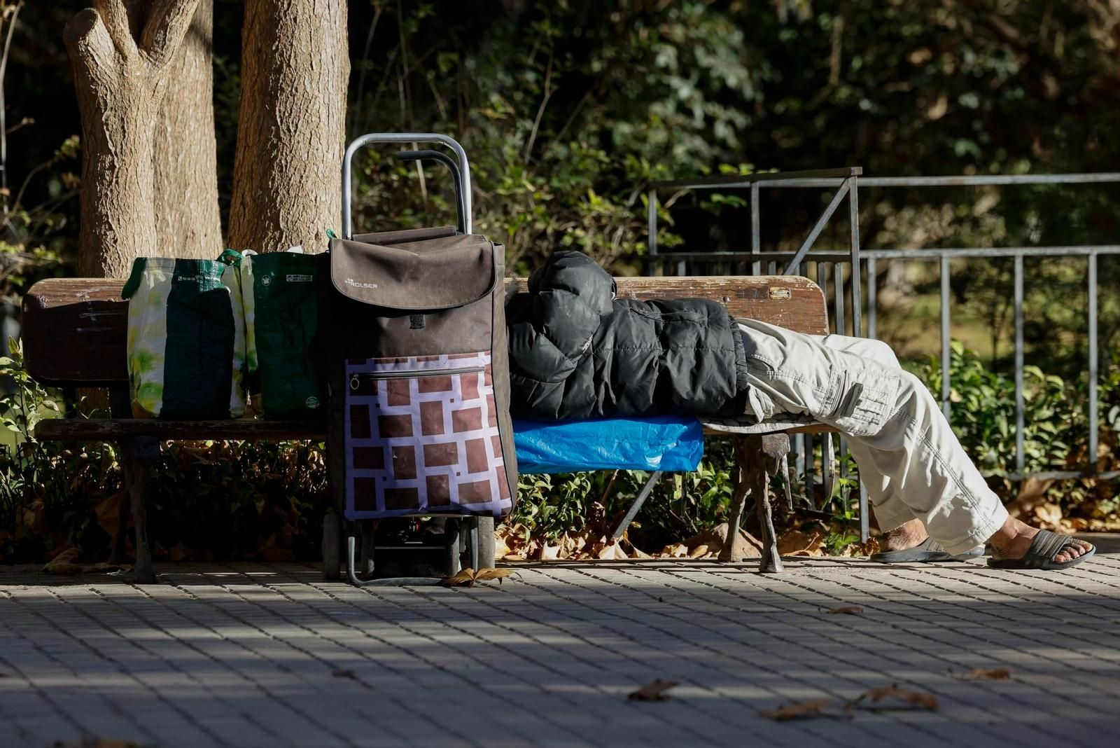 Una persona sin hogar descansa en un parque junto a sus pertenencias.