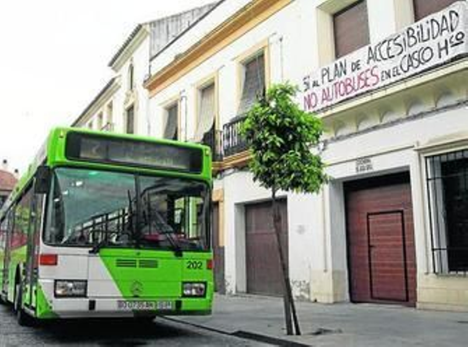 Un autobús de Aucorsa circula por la calle Alfaros delante de una pancarta de protesta vecinal.