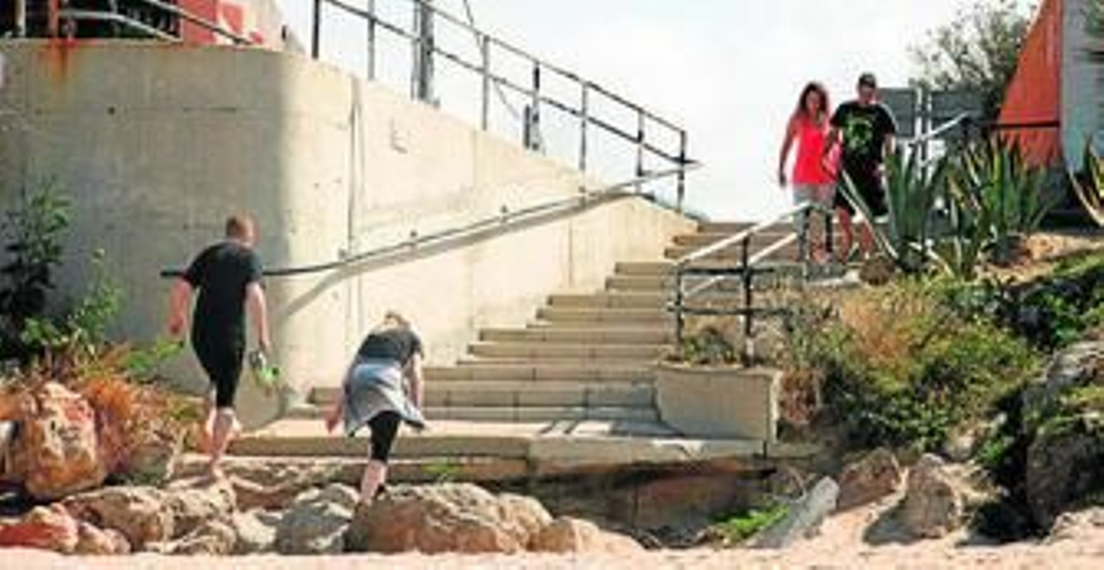 Unos usuarios de la playa de Zahora intentan acceder a la escalera por encima de las piedras que han aparecido.