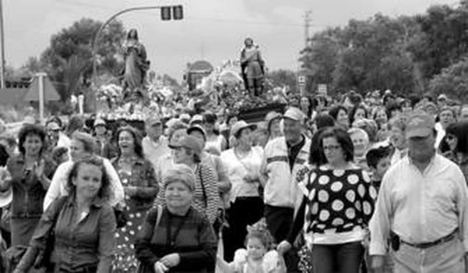 C¡entos de personas caminan delante de las imágenes de la Virgen y San Isidro Labrador.