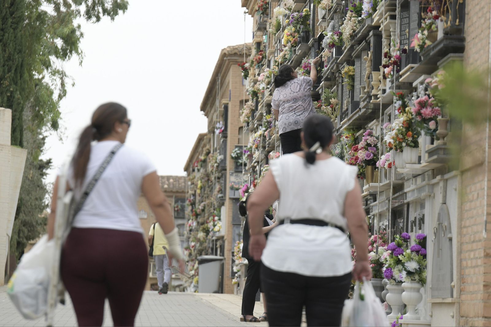 Dos mujeres contemplan como otra coloca flores en un nicho