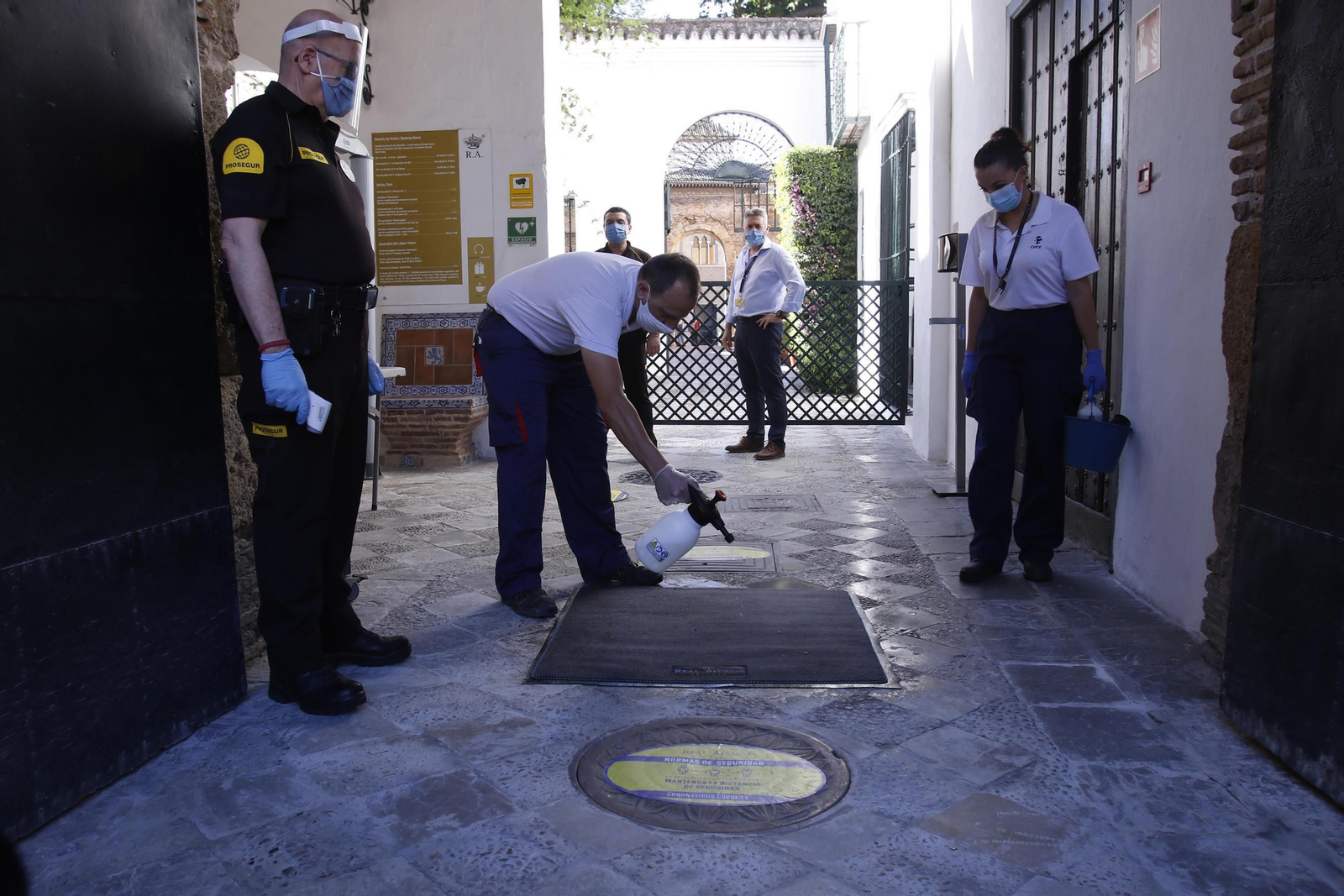 Un vigilante de seguridad observa como un empleado limpia el suelo de la Puerta del León tras la reapertura del Real Alcázar.