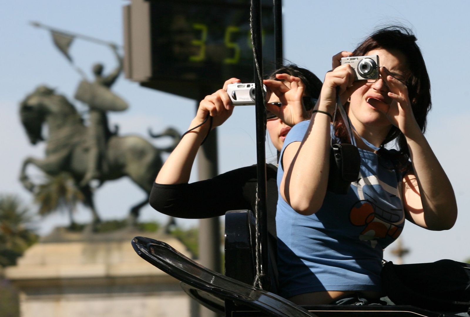 Dos turistas fotografían el termómetro de El Prado de San Sebastián marcando 35 grados.
