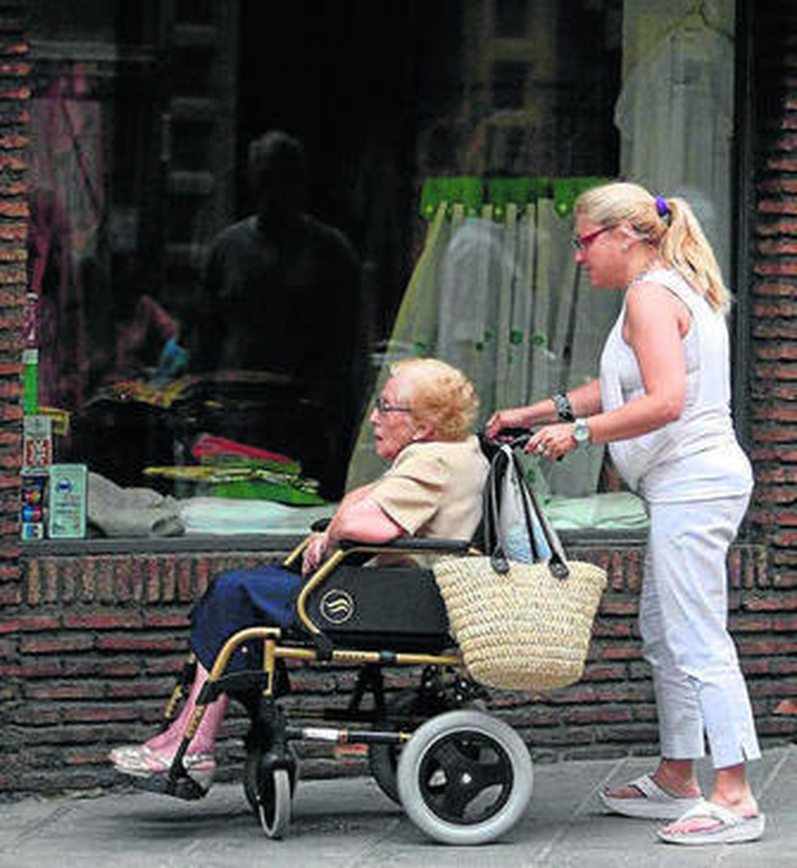 Una mujer traslada a una anciana en silla de ruedas.