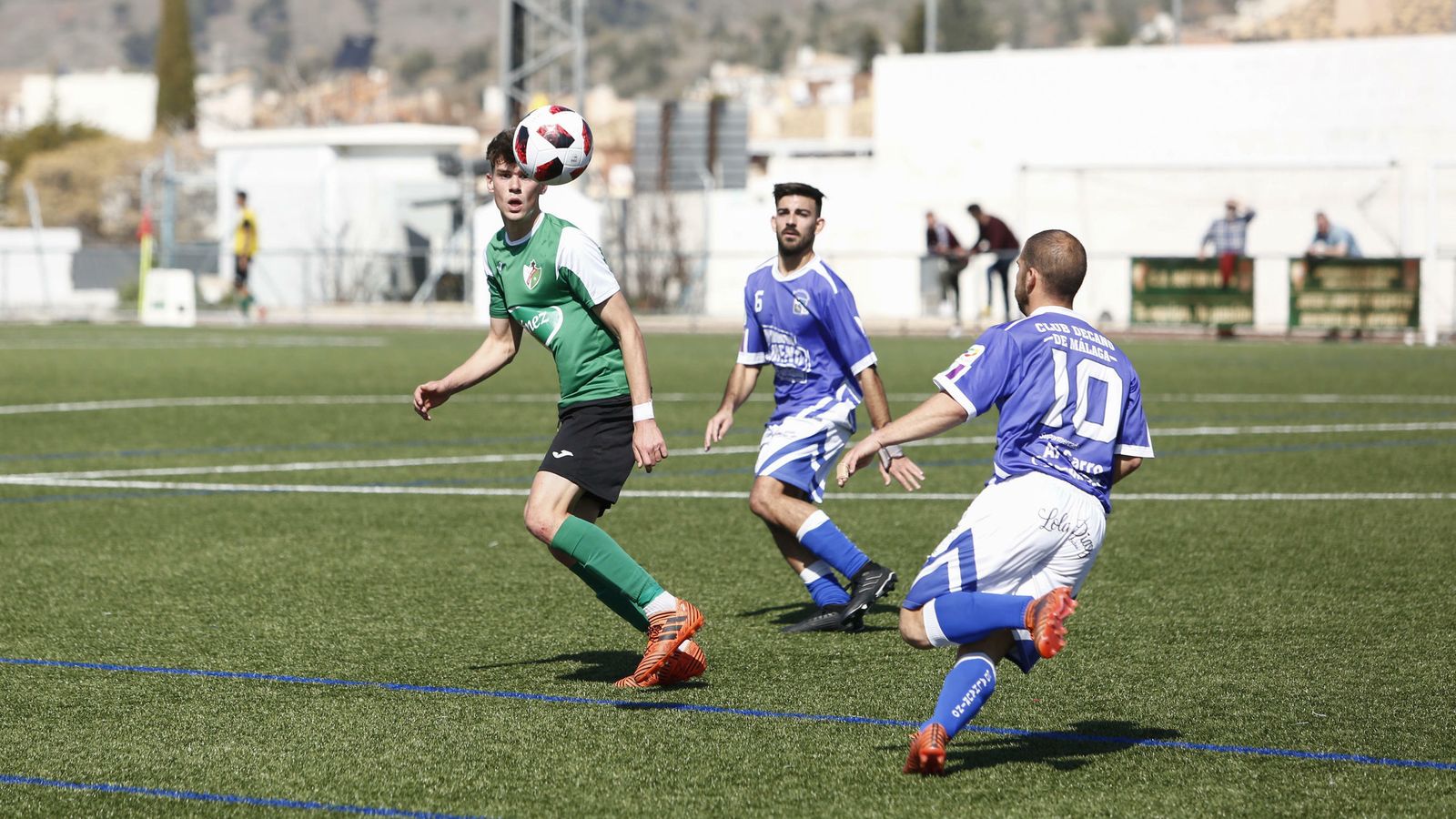 Un jugador del Huétor Vega mira el cuero rodeado de dos contrarios.